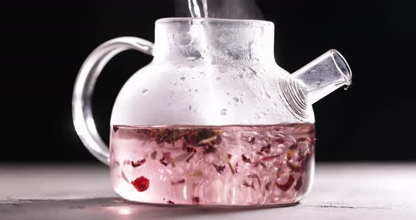 Process of Brewing Pink Flowers Tea in Glass Transparent Teapot at Dark Background