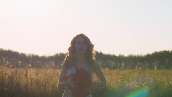 Redhead Young Woman in White Dress Throws Soft Hearts on Background of the Field