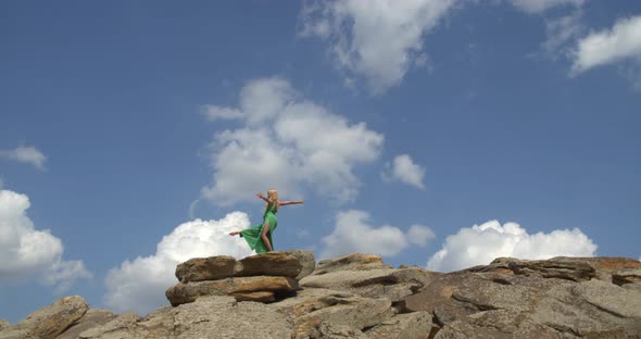 Sexy Woman in Green Dress is Dancing on Top of a Rocky Hill on a Sunny Day