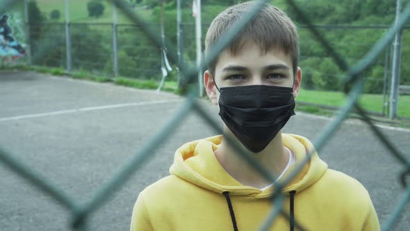 young man in a medical protective mask behind a metal fence. Black surgical mask. 