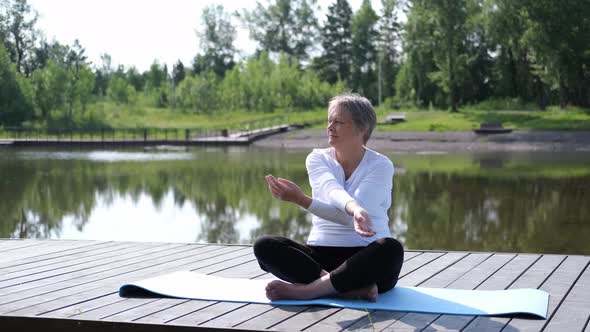 A Relaxed Athletic Mature Woman Does Yoga in the Park Near the Lake