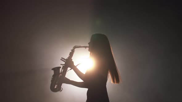 Young Beautiful Girl in a Dark Dress Plays on a Golden Shiny Saxophone on Stage