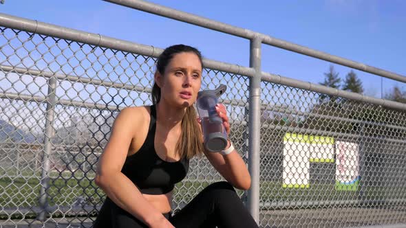Young athletic woman sitting fatigued drinks water after workout