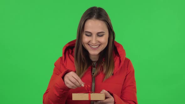 Portrait of Lovely Girl in a Red Down Jacket Is Opening the Gift and Disappointed. Green Screen