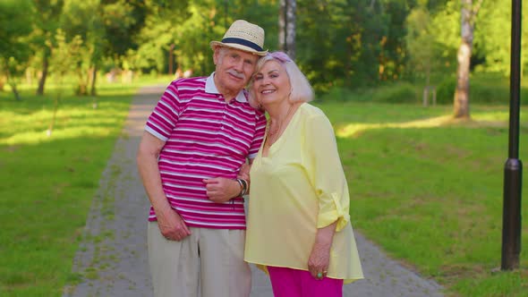 Senior Old Stylish Tourists Couple Grandmother Grandfather Walking in Summer Park and Making a Kiss