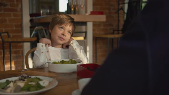 Little Boy Sits at a Wooden Table in a Cafe 