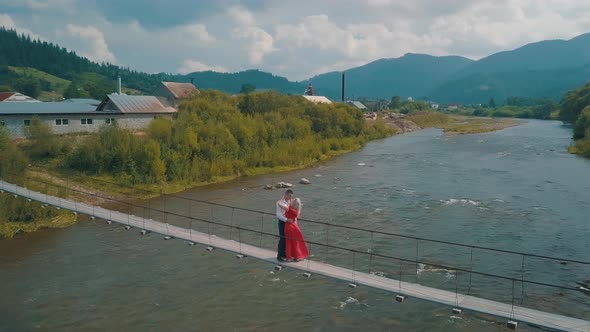 Сouple Stands on Bridge Over a Mountain River. Love of Man and a Woman