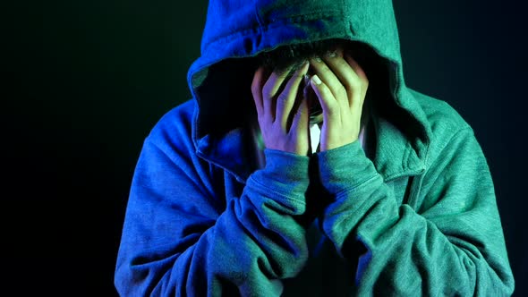 Sad Man in Hood Cover Face with Hands Isolated in Black