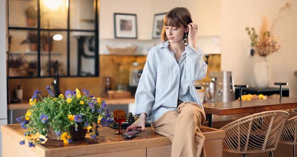 Woman Sits on a Kitchen Top with Phone at Beautiful Home