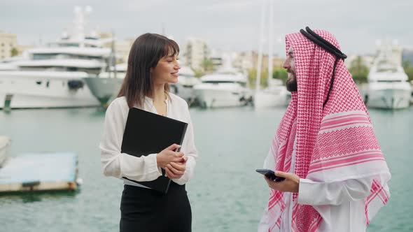 Arab Businessman Discussing Terms and Conditions for Yacht Charter with Female Broker in Port