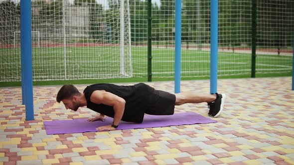 Man in Black Sportswear Doing Push Ups on Mat with Football Field on Background