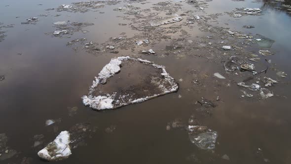 Large Dirty White Ice Floes Float on a Gloomy River