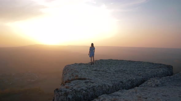 Beautiful young girl traveler go to the edge of a huge rock in the mountains