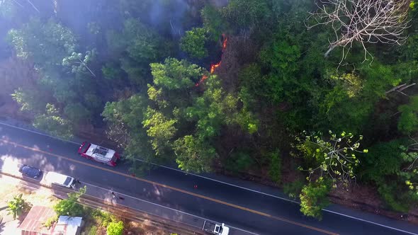 Aerial view of a firetruck at a tropical forest fire near a road and accommodation, in South America