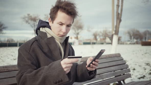 Men Paying Online with Credit Card and Smart Phone on Bench in Winter Season