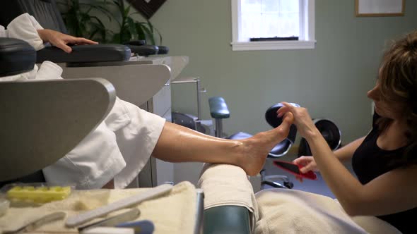 Pedicurist files her client's foot. Camera on slider tracking left to right.