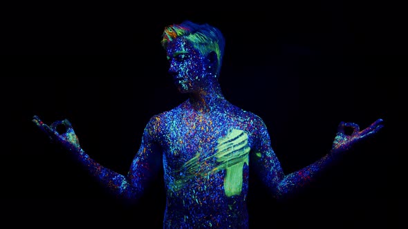 Young Man Painted in Different Colors with Fluorescent Paint is Standing in Studio Under Ultraviolet