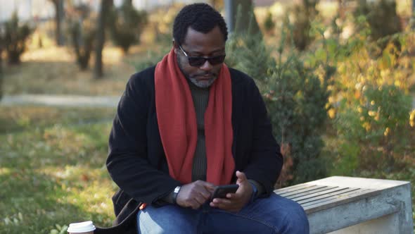 Serious African man typing by phone in park