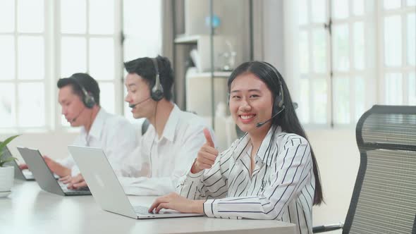 A Woman Of Three Asian Call Centre Agents Smile To Camera Then Thumbs Up