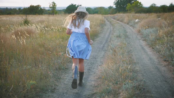 Little Girl in Rubber Boots Run in a Field in the Countryside.