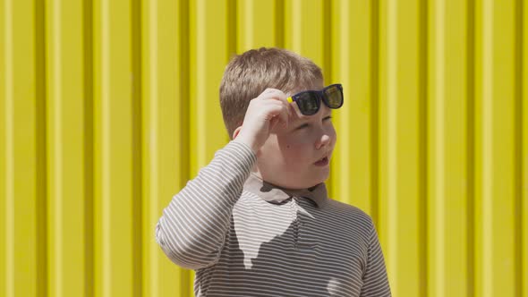 Boy Raises His Sunglasses and Looks Suspiciously Near Bright Yellow Ribbed Wall