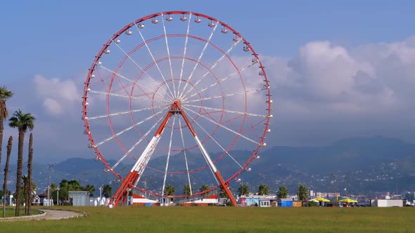 Ferris Wheel Against the Blue Sky with Clouds Near the Palm Trees in the Resort Town, Sunny Day