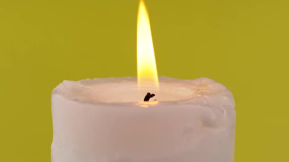 Burning White Candle with a Bright Flame on an Isolated Yellow Background