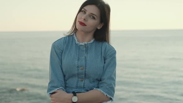Young smiling brunette woman with red lipstick in denim overalls  sits on sunlights