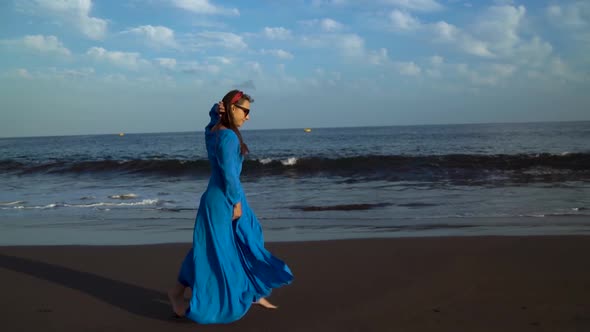 Woman in a Blue Dress Runs Along a Black Volcanic Beach
