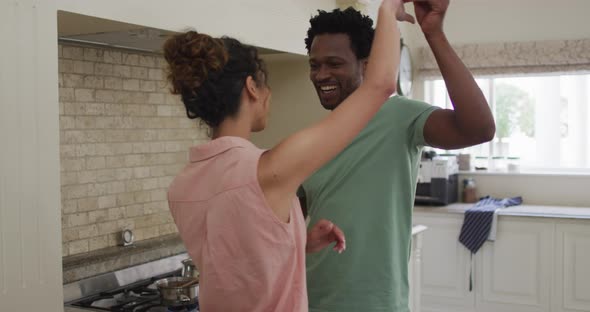 Happy biracial couple dancing together in kitchen