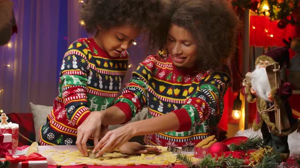 African American Mom and Little Daughter in Bright Holiday Sweaters Cut Festive Homemade Cookies