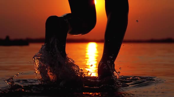 Silhouette of Legs of Boy Running Into the Water at Sunset and Creating Splashes. Slow Motion