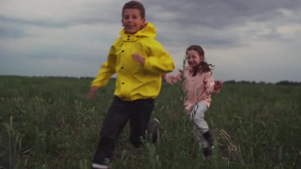 Small Cute Girl Running for Cheerful Boy Over Green Field Smiling Foreground in Slow Motion