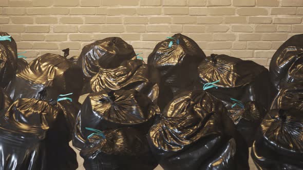 An endless pile of black plastic garbage bags against dirty brick wall loop. 4K