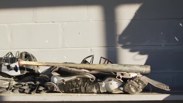 Pile of protective baseball pads, helmets and a baseball bat in the changing room at baseball pitch