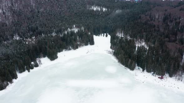 Isolated frozen volcanic crater lake in forest, Sfanta Ana, Romania, drone tilt down