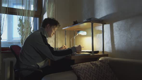 Student Businessman Working in a Dark Room with a Desk Lamp with Documents. The Student Solves