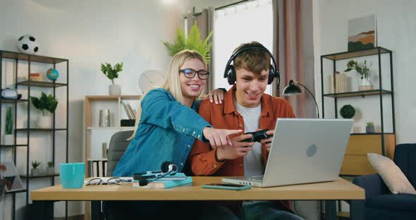 Young Guy in Headset Enjoying Video Games on Laptop Near Supporting Smiling girlfriend