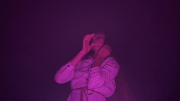 Slow ecstatic dance of young woman in white dress in darkness. Night club Pink light Low angle view