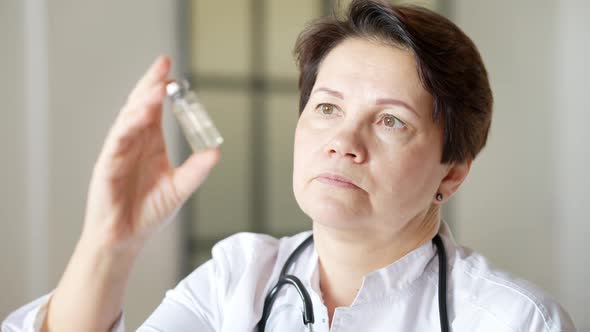 Closeup Portrait of Serious Female Doctor Holding Vaccine Jar and Looking at Camera