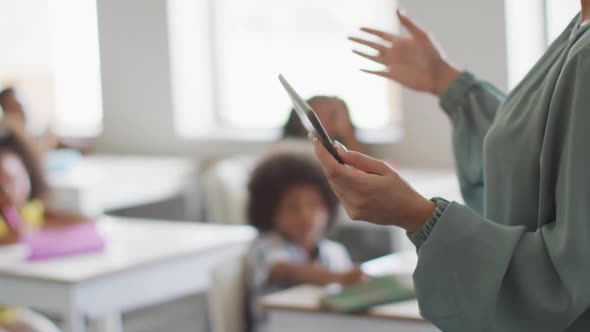 Video of hands of caucasian female teacher holding tablet in class of diverse pupils