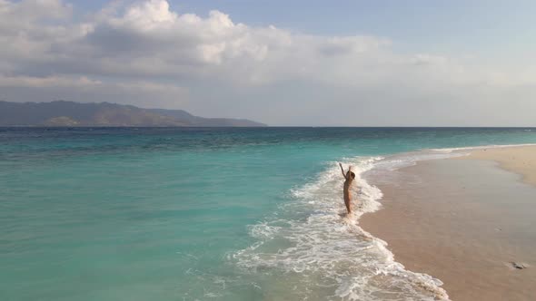 Girl raising arms on beautiful tropical island during sunny day on Lombok.Aerial drone circle shot.