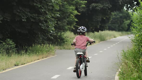 Child riding bicycle on the bike path at rain. Kid in helmet learning to ride at summer