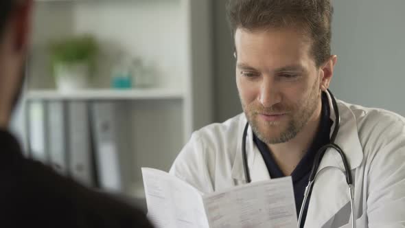 Attentive Male Doctor Reading Medical Test Result and Prescribing Vitamins