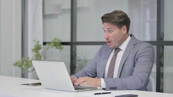 Middle Aged Man Reacting to Loss While using Laptop in Office