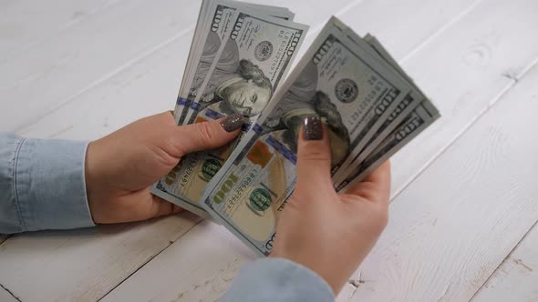 Closeup of a Young Woman Counting Dollars on a Light Wooden Background