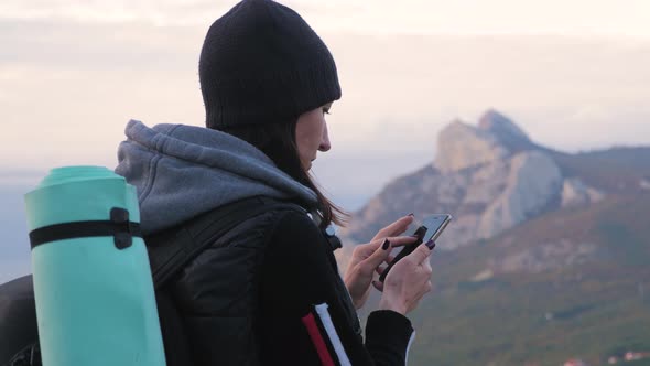 Young Girl Traveler with Backpack Using Smartphone Digital Device Blurred Top Mountain Background