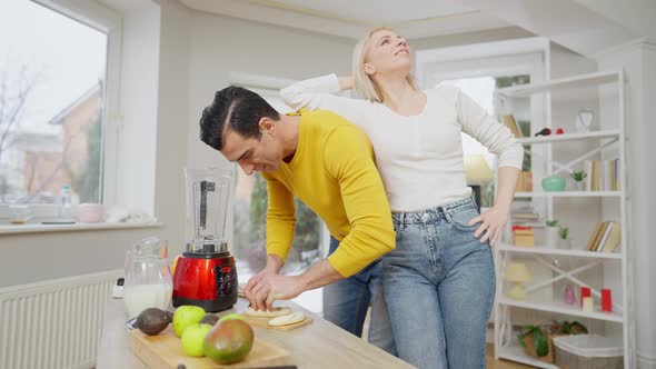Cheerful Beautiful Woman Leaning on Man Cutting Banana for Healthful Dieting Smoothie