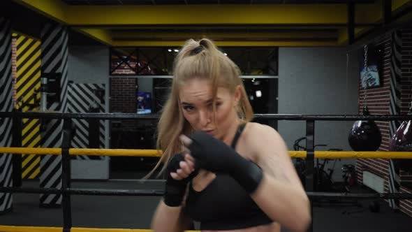 A Woman with Boxing Bandages on Her Hands Practices Punches in the Boxing Ring