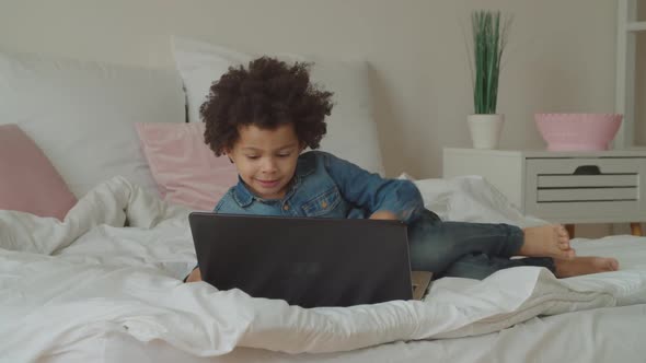Multiethnic Child Typing on Laptop Keyboard on Bed